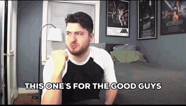 a man is sitting in a bedroom with his fist in the air and says `` this one 's for the good guys ''