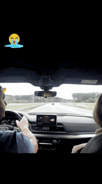 a man and a woman are driving down a highway with a crying face on the dashboard