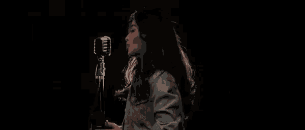 a woman is singing into a microphone in a dark room .