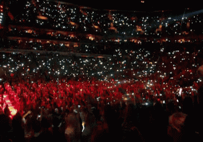 a crowd of people are gathered in a stadium with their phones in the air
