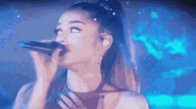 ariana grande is singing into a microphone on a stage in front of a blue background .