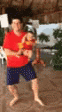 a man in a red shirt and blue shorts is holding a baby .