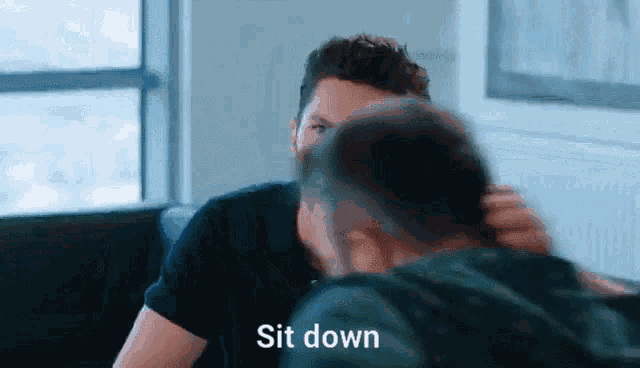 two men are sitting next to each other and one of them is holding the other 's hair .