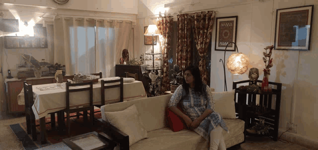 a woman sits on a couch in a living room with a table and chairs