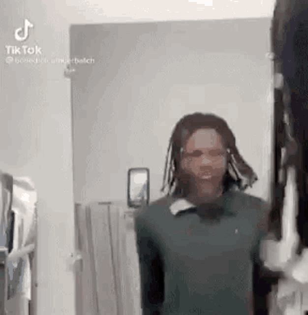 a man with dreadlocks is standing in front of a mirror and smiling .