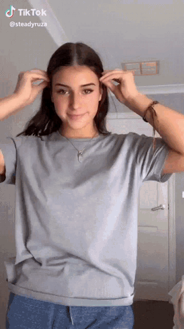 a woman is wearing a grey t-shirt and blue pants and has a tiktok account