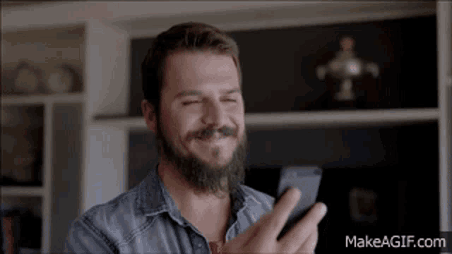 a man with a beard is smiling while looking at a cell phone