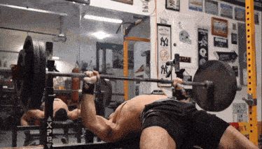 a man lifting a barbell in a gym with a ny yankees banner on the wall behind him