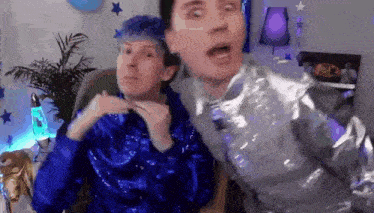 a couple of men are sitting next to each other in a room . one of the men has blue hair .
