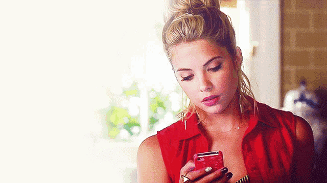 a woman in a red shirt is holding a red cell phone
