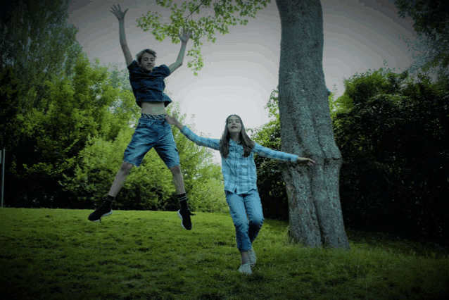 a boy and a girl are jumping in the air while standing next to a tree