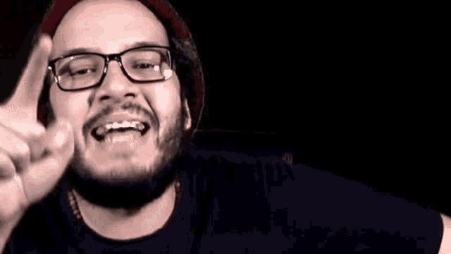 a man with a beard wearing glasses and a hat is making a funny face .