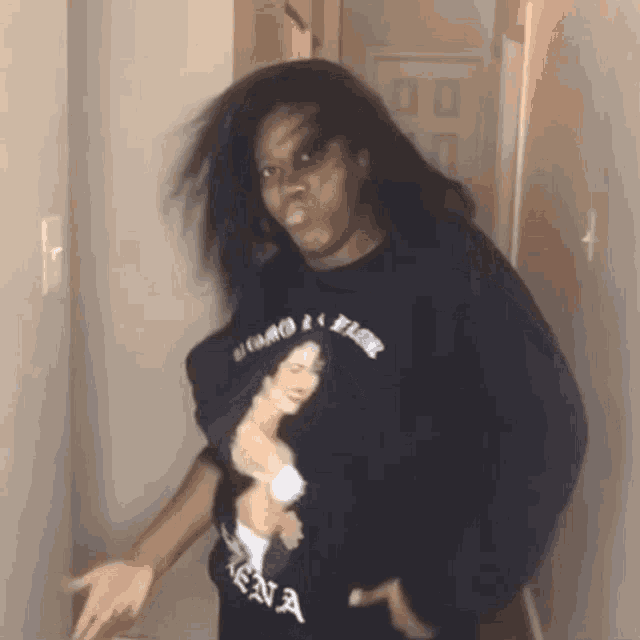 a woman wearing a shirt with a picture of a woman on it is standing in a hallway with her hair blowing .