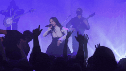 a woman singing into a microphone while a man plays a guitar in the background