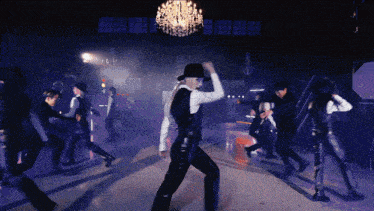 a group of people dancing in a dark room with a chandelier in the background