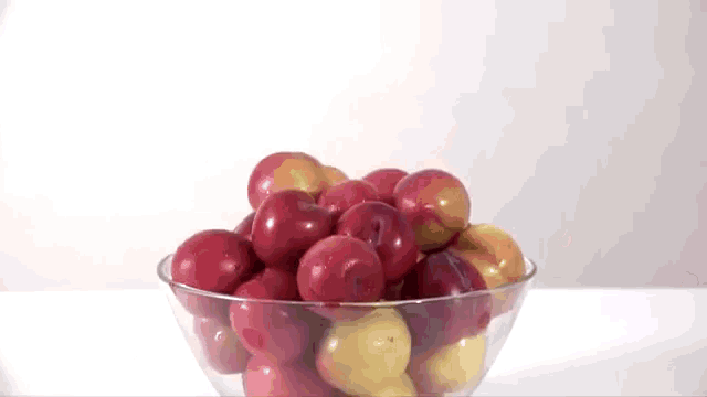 a glass bowl filled with red and yellow plums .