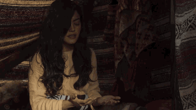 a woman sitting in a dark room with her eyes closed and her hands outstretched