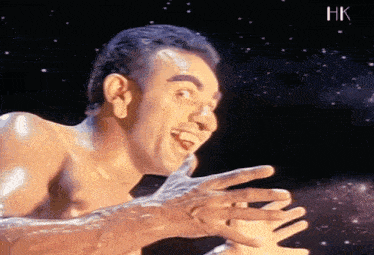a shirtless man is making a funny face with his hands outstretched in front of a starry sky .