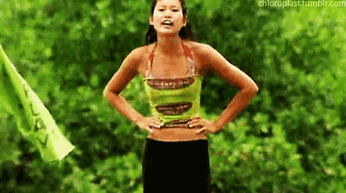 a woman in a green top and black skirt is standing with her hands on her hips .
