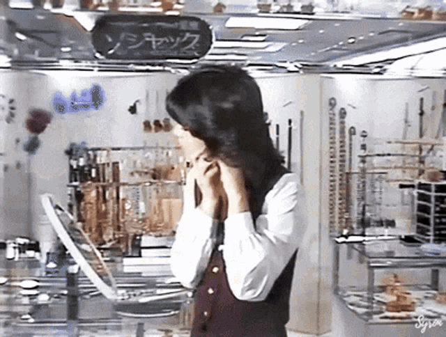 a woman looks at herself in a mirror in a store with a sign that says ' syra '