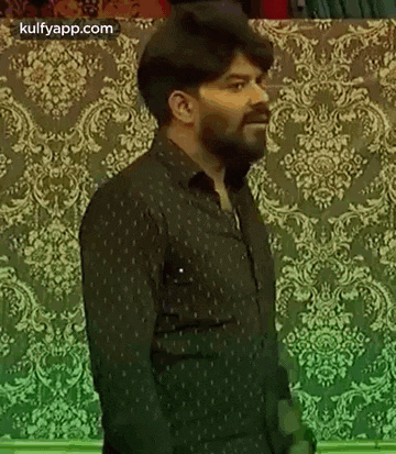 a man with a beard wearing a black shirt is standing in front of a wall .