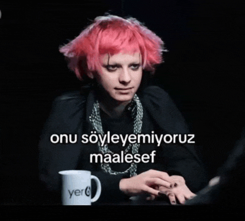 a woman with pink hair is sitting at a table with a mug that says yer