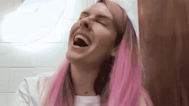 a woman with pink hair is laughing in a bathroom
