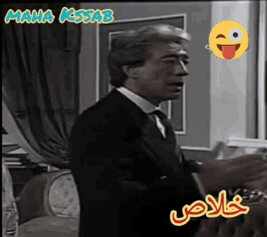 a man in a suit and tie is standing in front of a window with the name maha kissab on the bottom right