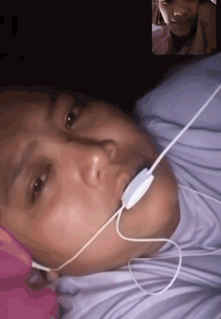 a woman wearing headphones is laying in bed with another woman on a video call