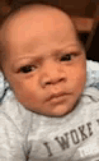 a baby wearing a i woke shirt is making a funny face .
