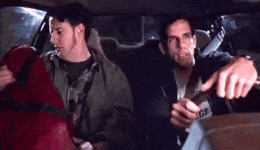 two men are sitting in the back seat of a car . one of them is pointing at something .