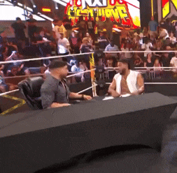 two men are sitting at a table in front of a crowd with a sign that says nxt on it