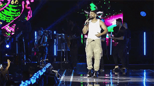 a man in a white tank top is singing into a microphone