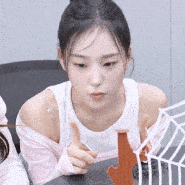 a woman in a white tank top is sitting at a table with a spider web .