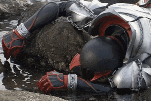 a superhero is chained to a rock in the water and has the letter o on his gloves