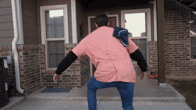 a man in a pink shirt and blue jeans is standing in front of a brick house