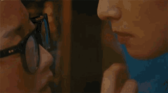 a man and a woman are kissing in front of a mirror . the man is wearing glasses .