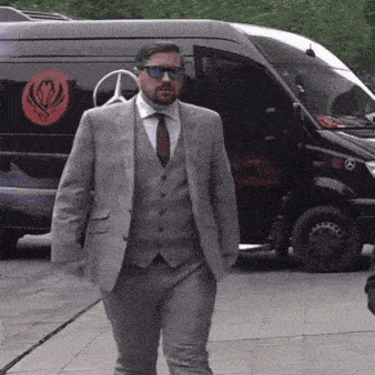 a man in a suit and tie stands in front of a black mercedes van