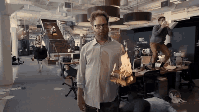 a man holding a burning piece of wood in an office with a sign on the wall that says buzzfeed