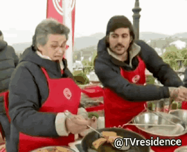 a man and a woman in red aprons are preparing food in a kitchen .