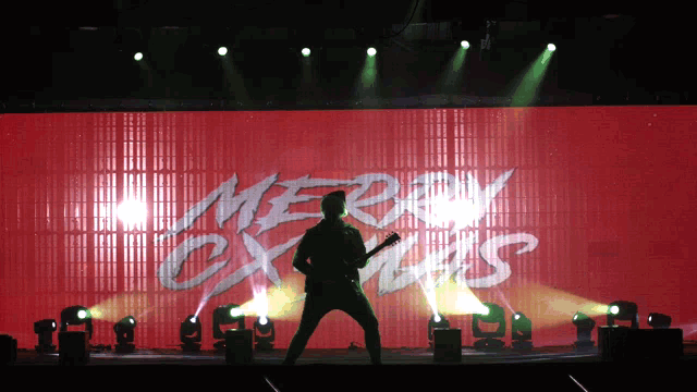 a man playing a guitar in front of a merry christmas screen