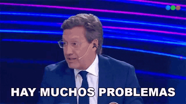 a man in a suit and tie is talking into a microphone and says hay muchos problemas