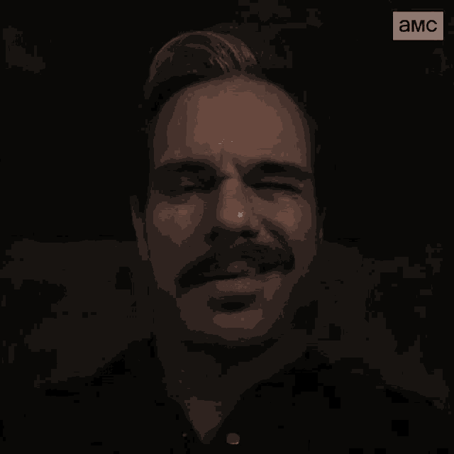 a man with a mustache is smiling and saying adios in a dark room .
