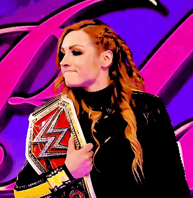 a woman with red hair is holding a wrestling championship belt in front of a pink and purple background .