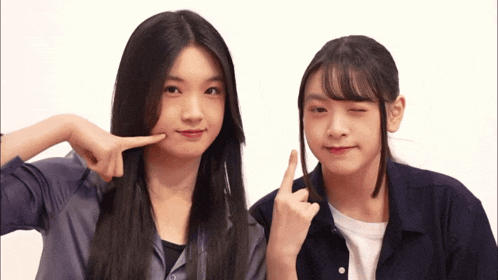 two girls are posing for a picture and one of them is pointing at her face