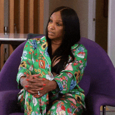 a woman in a green pajama set sits in a purple chair with her hands folded