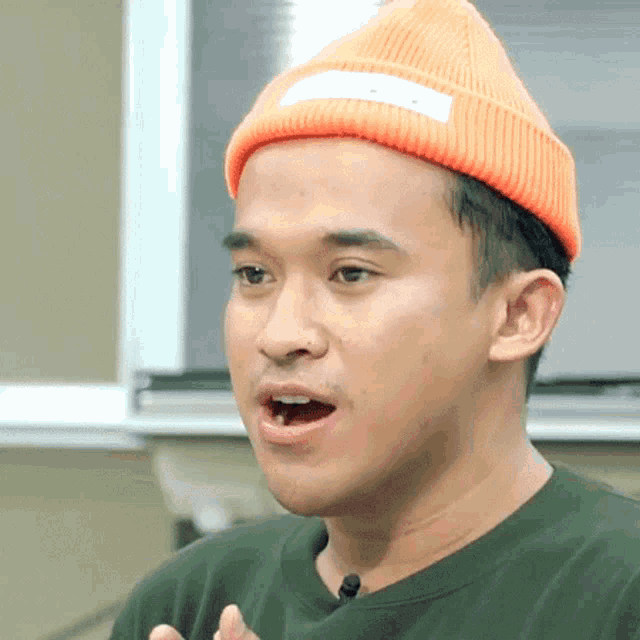 a man wearing an orange beanie and a green shirt is making a face