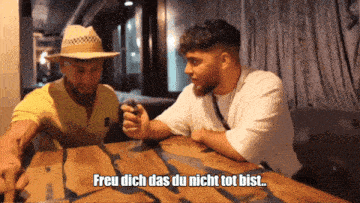 two men sitting at a table with the words " frei dich das du nicht tot bist " written below them