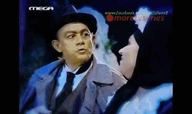 a man in a suit and tie is talking to a woman in a black hat on a screen that says mega