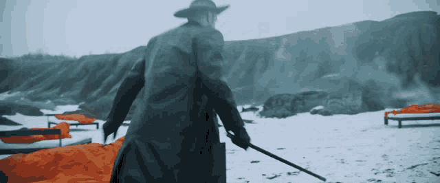 a man in a black coat and hat is walking in the snow holding a cane
